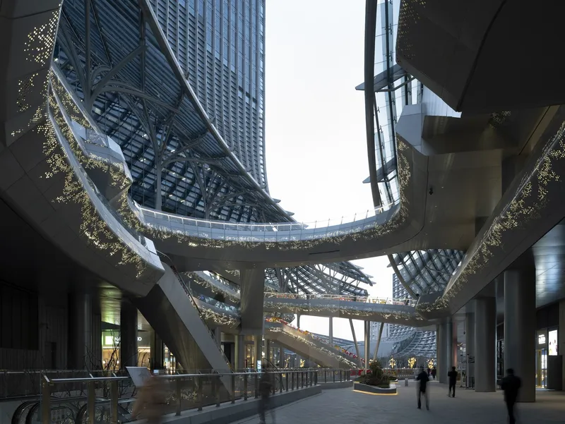 Ground floor passage beneath curved elevated walkways with suspended planters and tower above