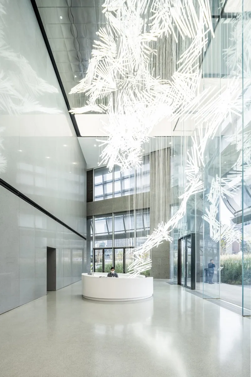Double-height lobby with terrazzo floor, white sculptural installation and reception desk beneath glazed curtain wall