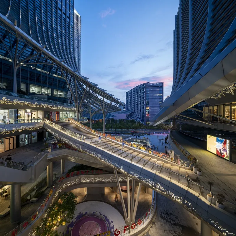 Multi-level pedestrian bridges and plaza connecting tower buildings at dusk with pink sky