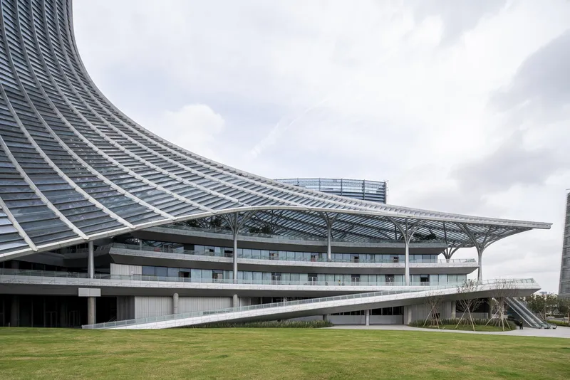Sweeping steel and glass canopy over horizontal building volumes adjacent to green lawn