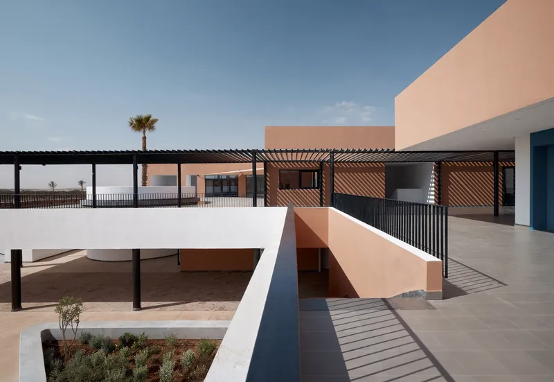 Elevated courtyard with timber pergola, planted beds, and connecting bridges between terracotta volumes