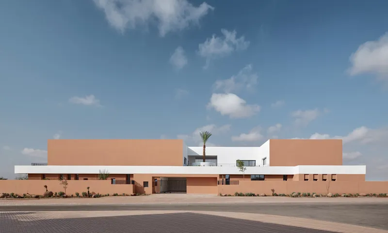 Frontal view of the horizontal composition with layered terracotta and white volumes under a clear sky