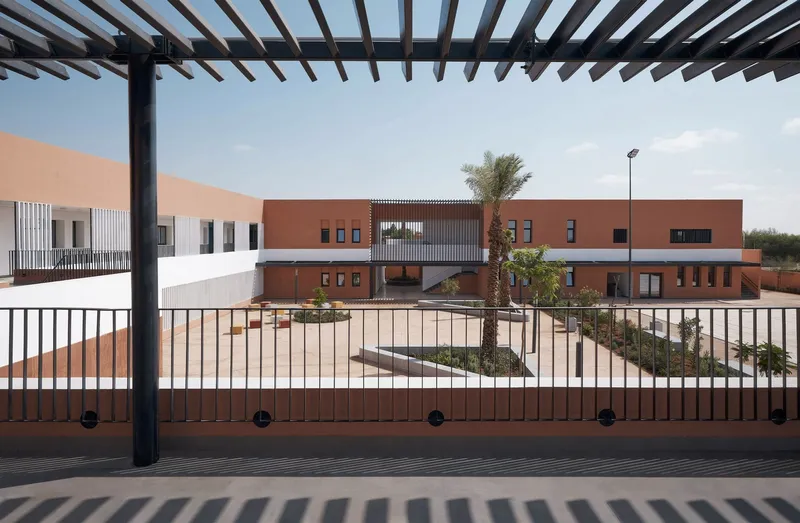 Landscaped courtyard seen through metal railings and a timber pergola with palms and planted beds in afternoon sun