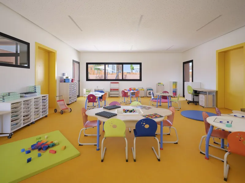 Kindergarten classroom with yellow rubber flooring, storage cabinets, and windows framing exterior planting