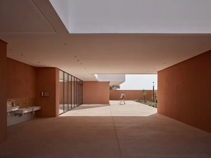 Covered courtyard with terracotta-finished walls and ceiling as a child walks through sunlit space