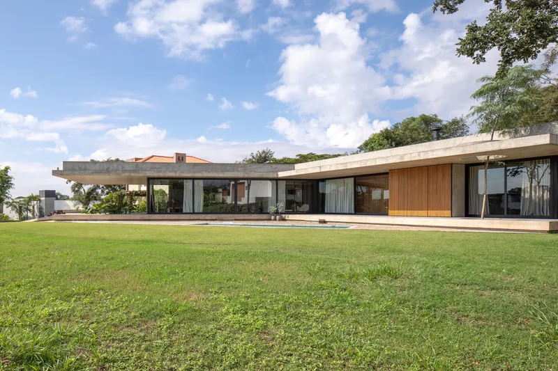 Long horizontal volume with concrete roof plane and timber cladding spanning across a manicured lawn