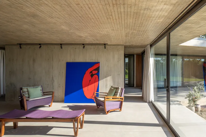 Covered terrace with board-formed concrete ceiling and timber louvers framing a vibrant red and blue artwork