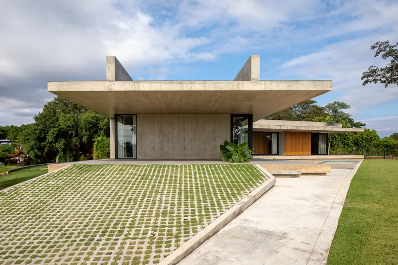 Elevated concrete canopy with timber-clad volume and gridded grass pavers leading to a reflecting pool