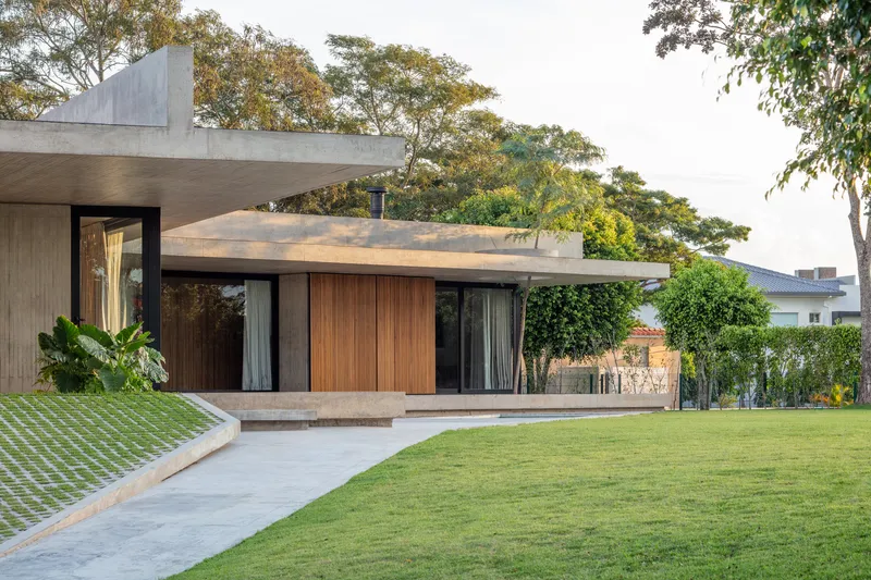 Timber-clad facade with full-height glazing beneath a cantilevered concrete slab surrounded by mature trees