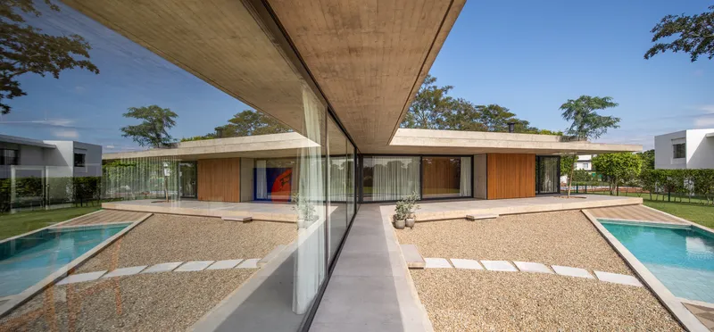 Glass-enclosed courtyard with gravel surface linking two pools beneath a cantilevered concrete soffit