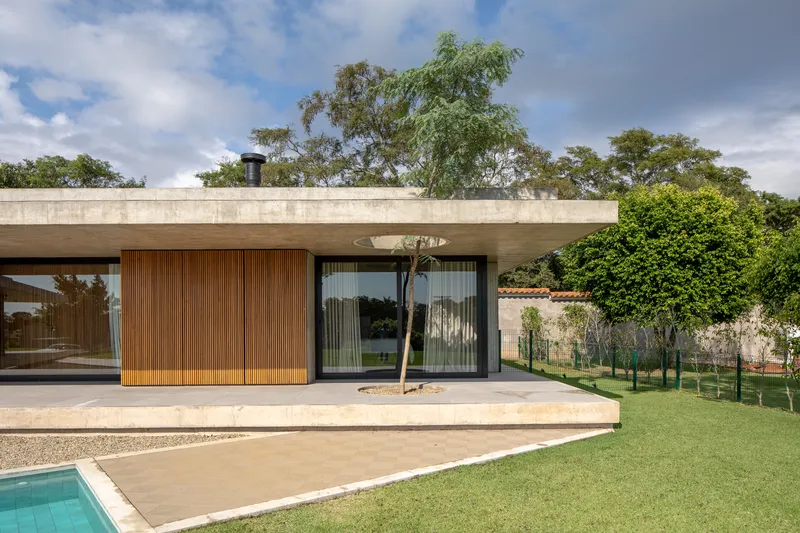 Horizontal concrete volume with vertical timber cladding panels and full-height glazing facing a lawn