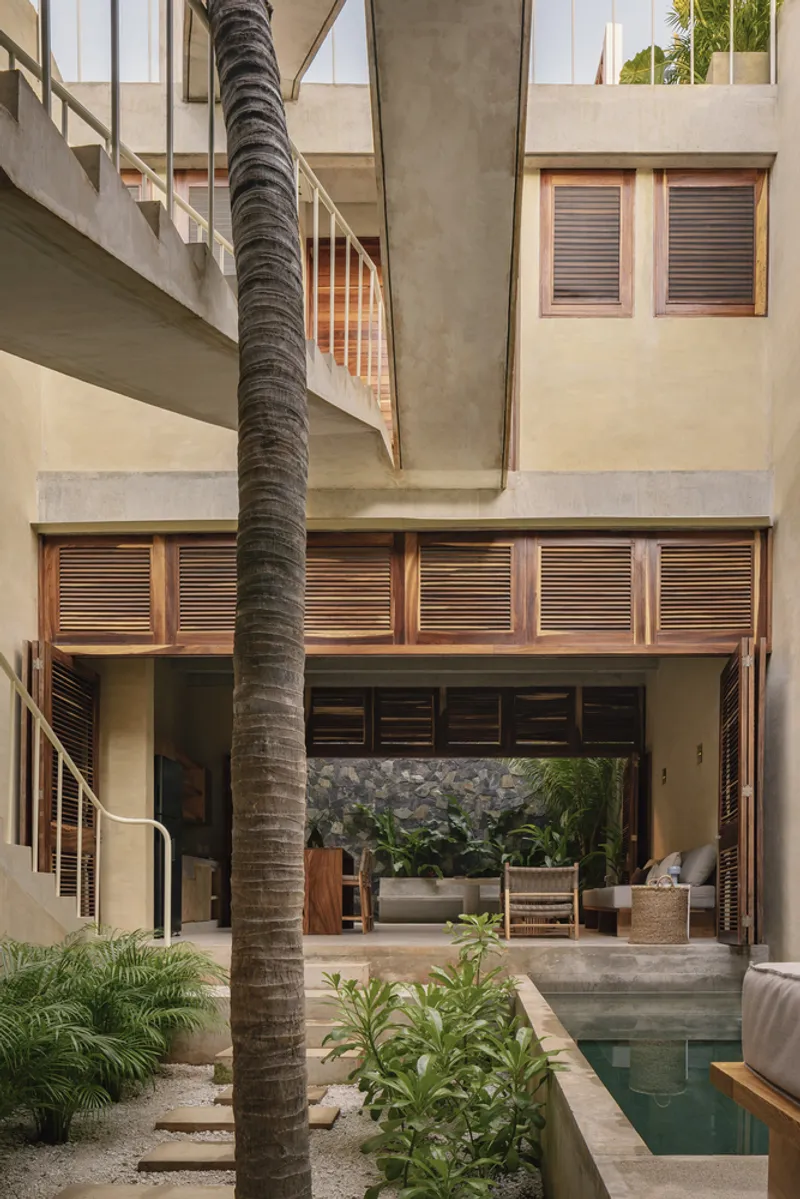 Courtyard with narrow lap pool alongside a tall palm tree and louvered wood shutters at dusk