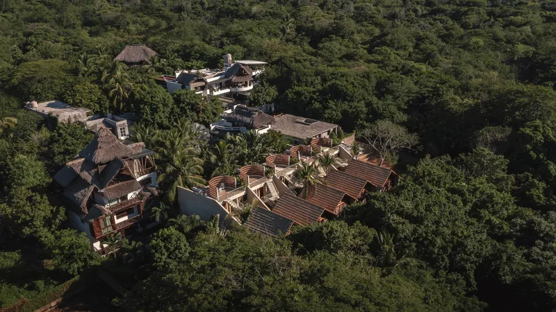 Drone view of the compound with thatched and tiled roofs scattered across a densely forested hillside