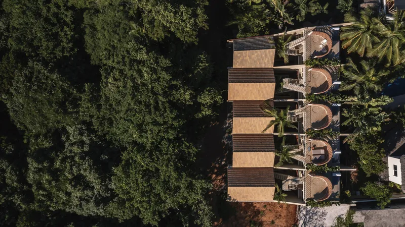 Aerial view of five timber-roofed units in a row with circular openings surrounded by dense tropical canopy