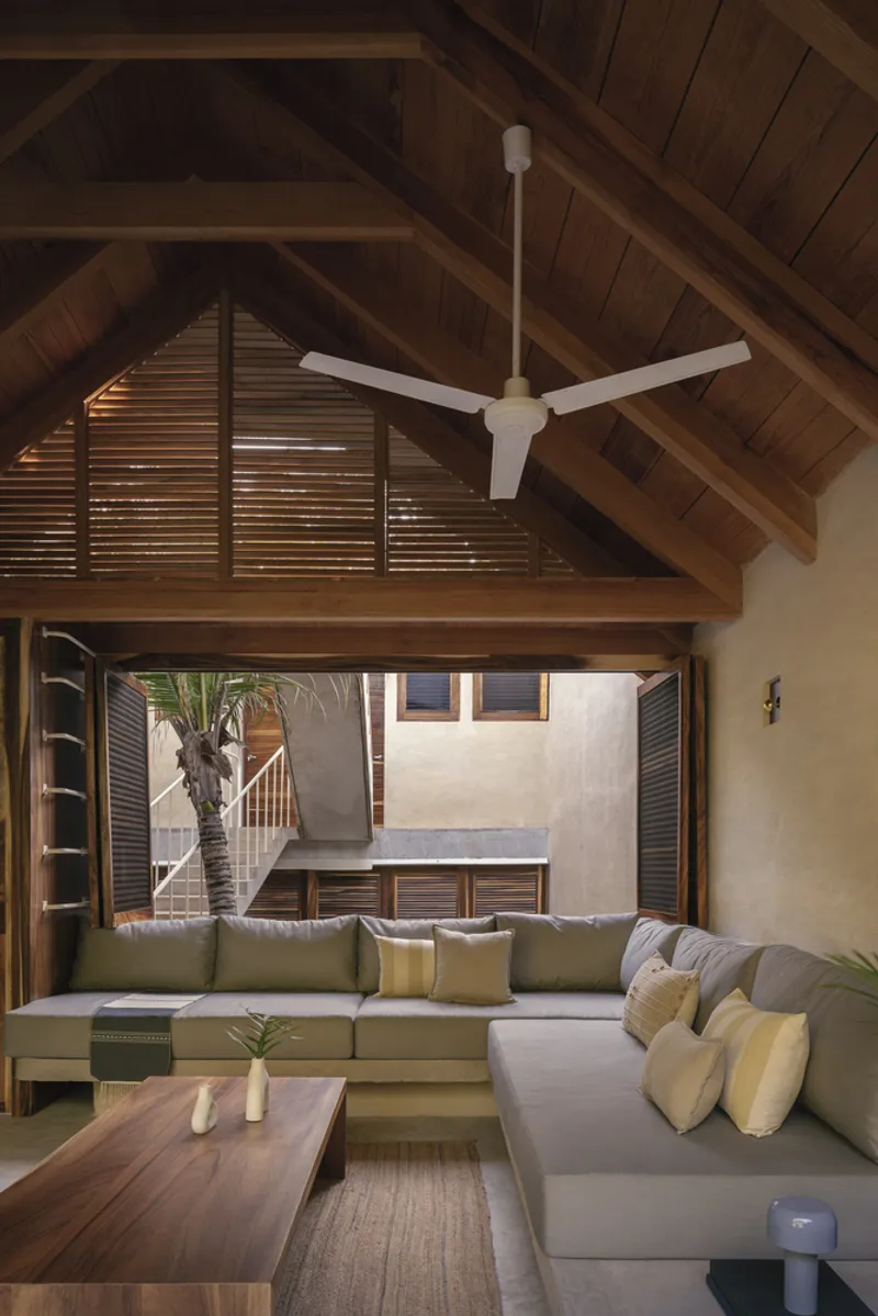 Living room with exposed timber gable ceiling and louvered doors opening to courtyard staircase beyond
