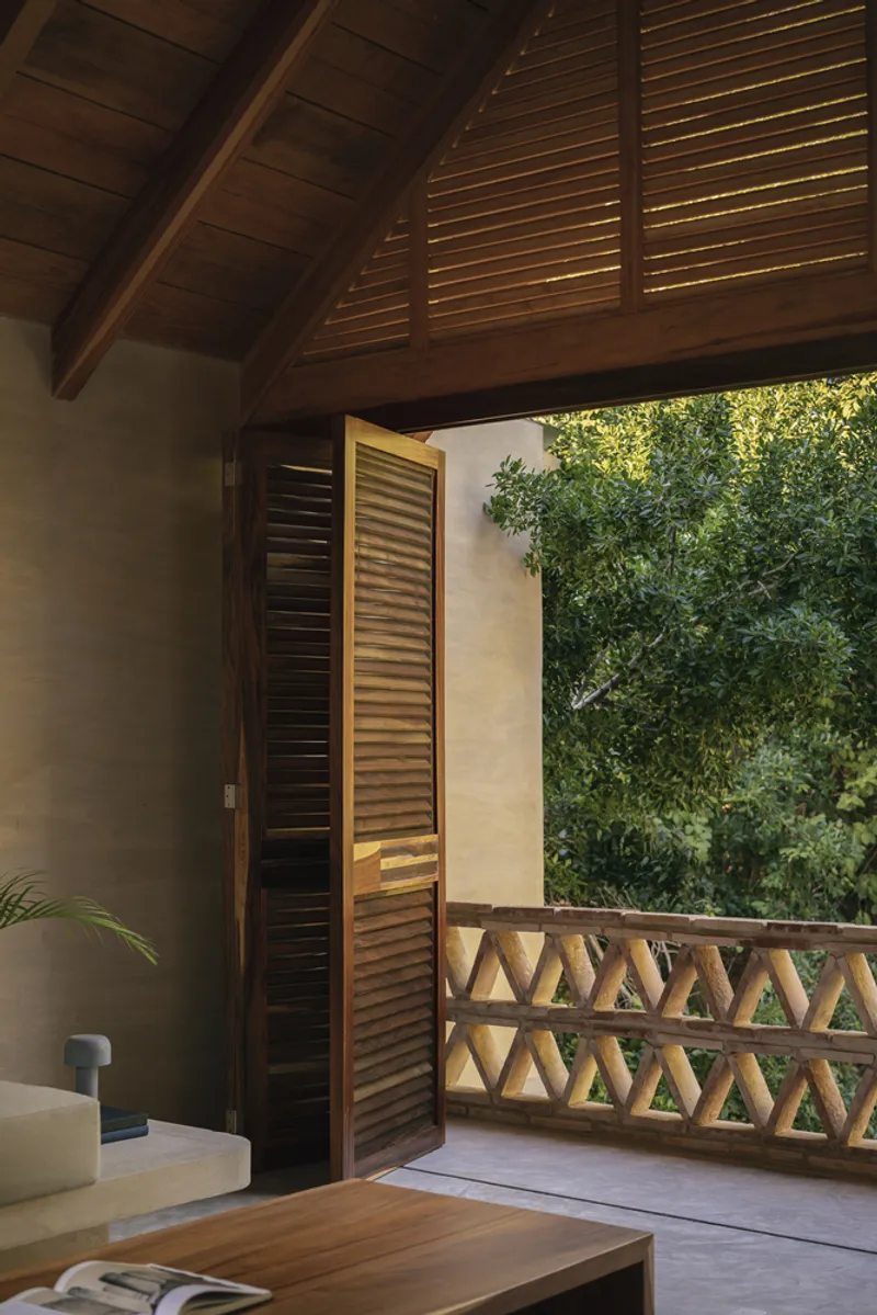 Covered balcony with timber louvered doors and triangular lattice railing overlooking dense greenery
