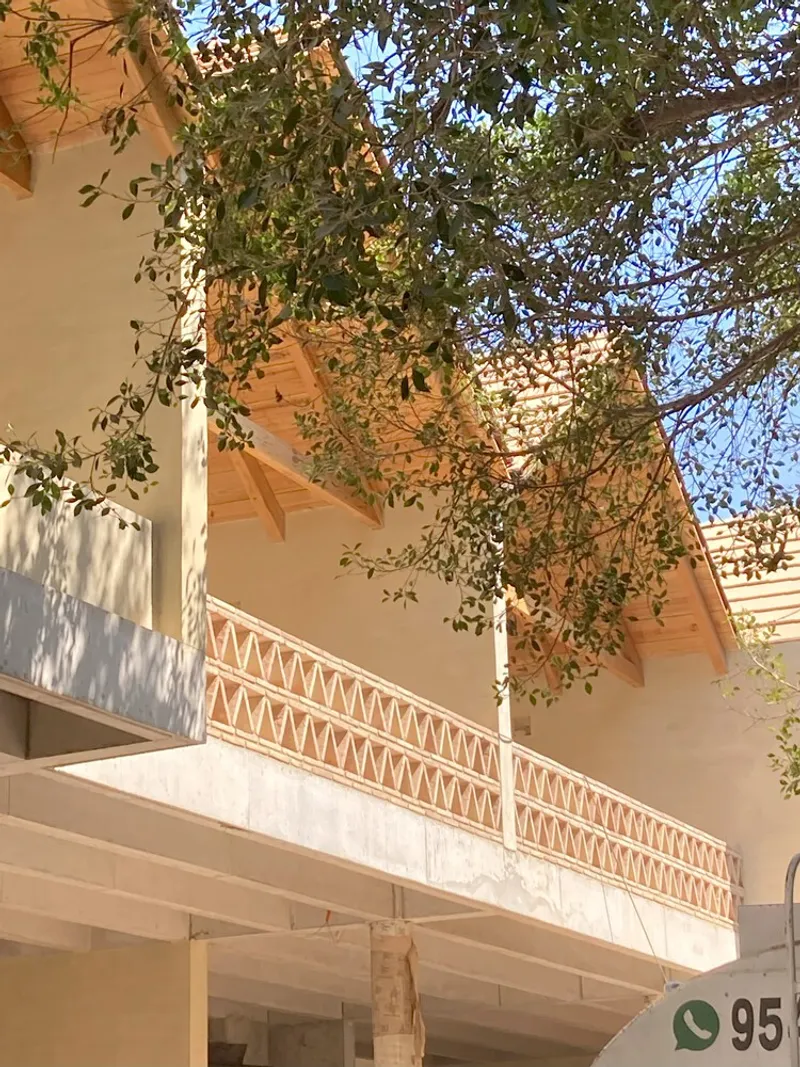 Upper-level balcony with terracotta triangular screen beneath pitched timber roof and overhanging tree branches
