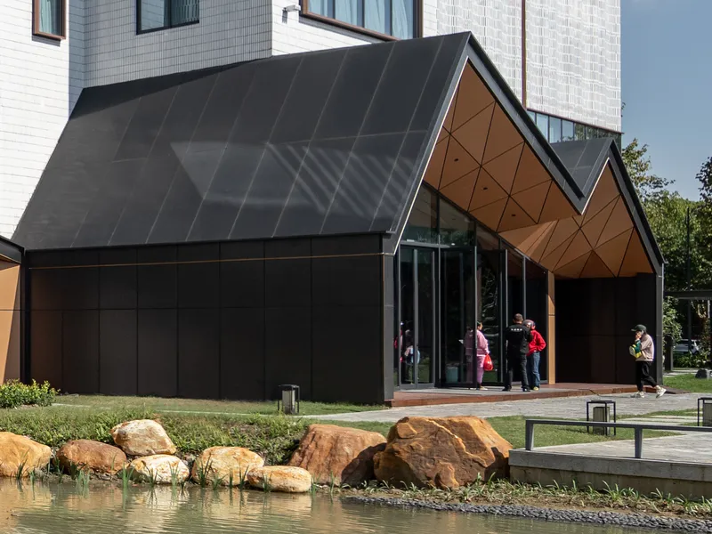 Black-clad gabled entrance with geometric timber gable end beside a shallow reflecting pond