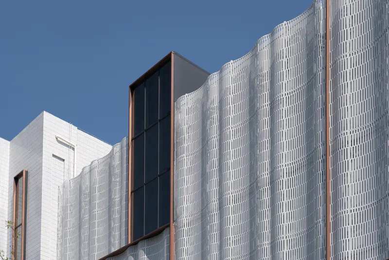 Vertical ribbed metal cladding with copper-framed glazed slot against a clear blue sky