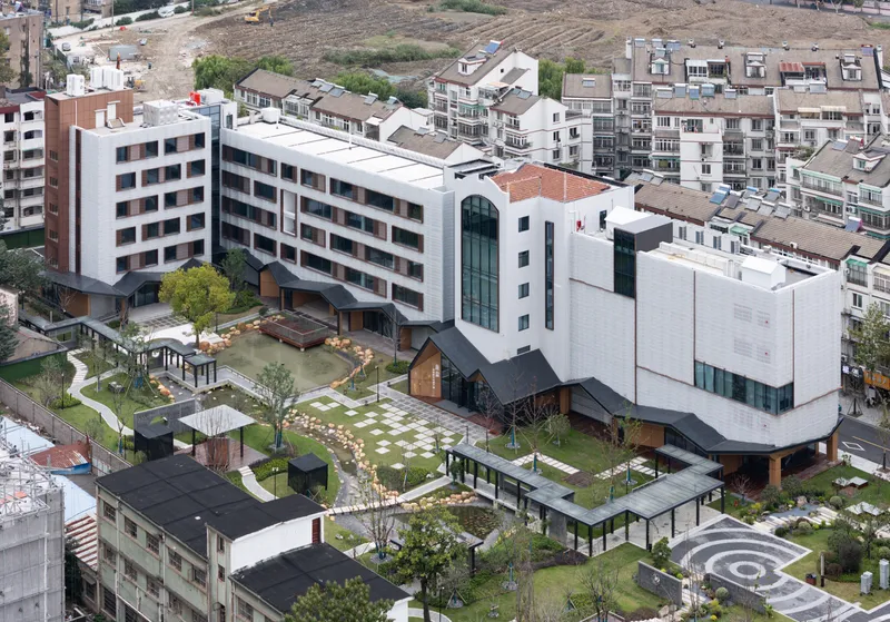 Aerial view of the campus with gabled pavilions, pond, and white residential tower beyond