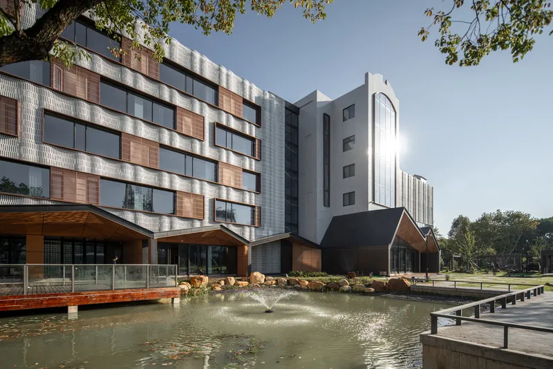 Rear facade with mixed cladding materials overlooking a landscaped pond with wooden deck and stone edging