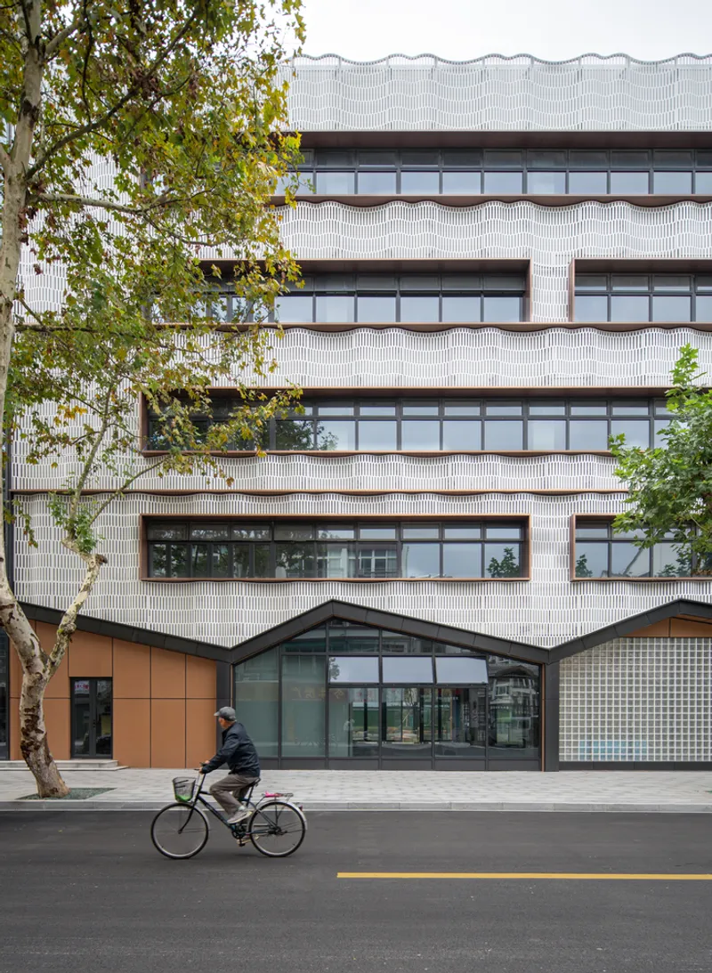 Street view of the white ribbed tile facade with horizontal window bands and a cyclist passing in front