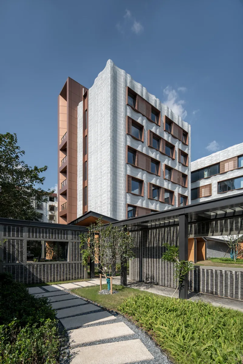 Tower volume with copper window frames set behind a low perforated screen wall enclosing a courtyard garden with stepping stones