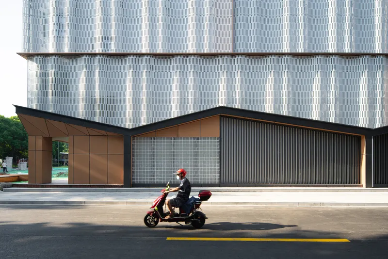 Ground floor facade with copper panels and glass block screen as a scooter rider passes on the street