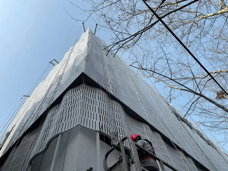 Upward view of the triangular white facade with vertical fins beneath bare winter branches