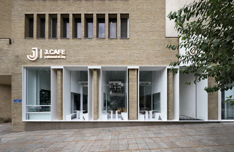 Street-facing facade with ribbed brick columns framing floor-to-ceiling glazing and cafe seating with a tree at right