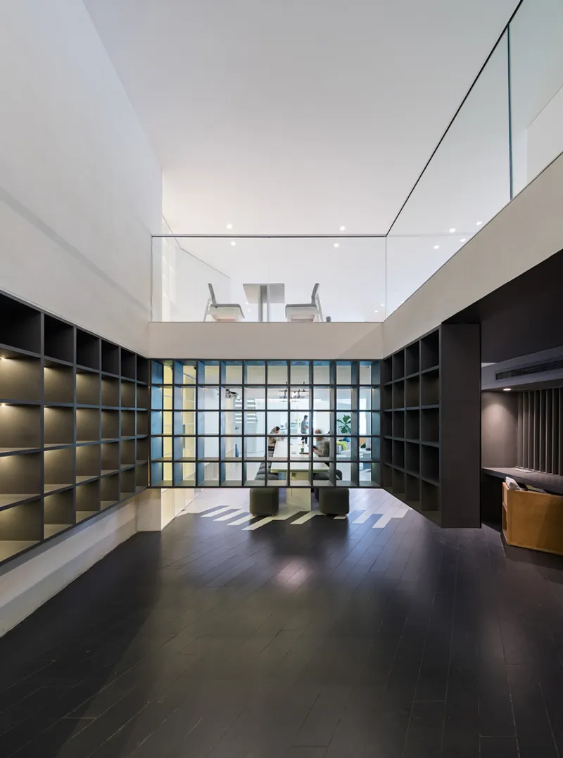 Double-height interior room with gridded display shelving and a glass block wall looking toward the upper mezzanine