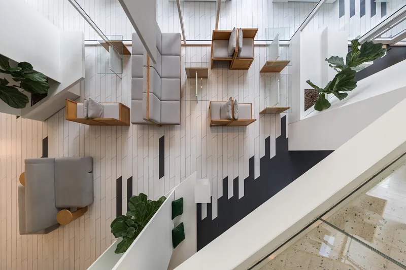 Top-down view of a seating area with floating timber benches suspended from cables above white vertical slat wall
