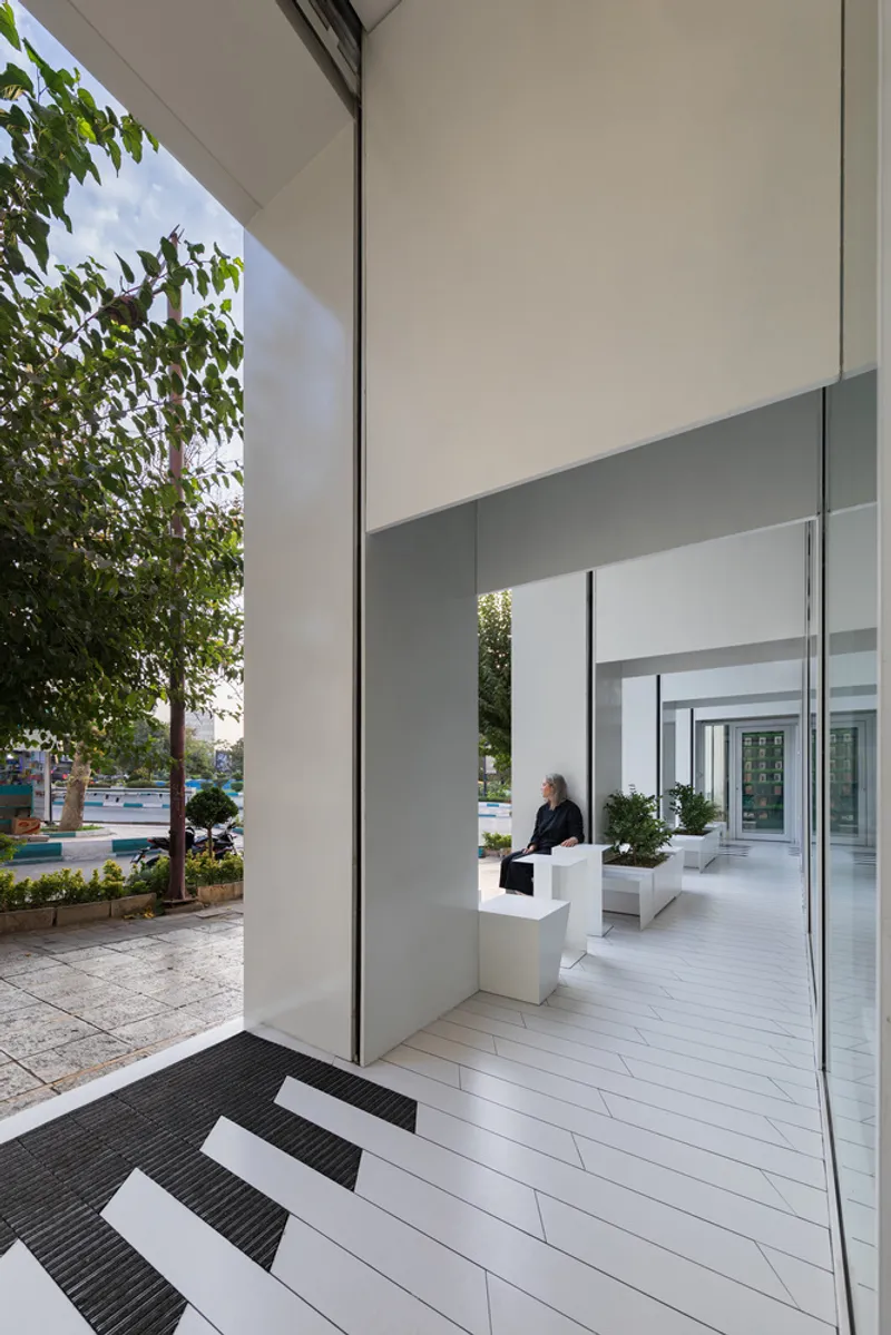 Entrance threshold with white tiled flooring and glass walls opening to a street with trees