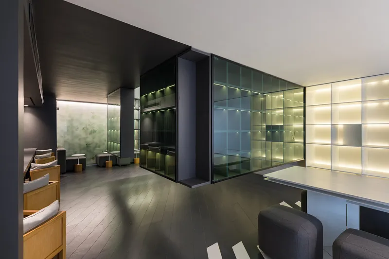 Interior lounge with backlit green glass paneling and dark wood flooring beneath a black ceiling