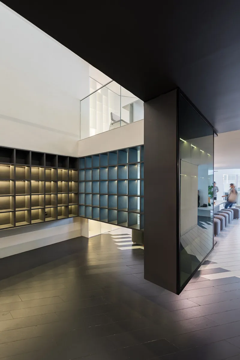 Double-height lobby with backlit grid walls in gold and green tones beside a dark volume