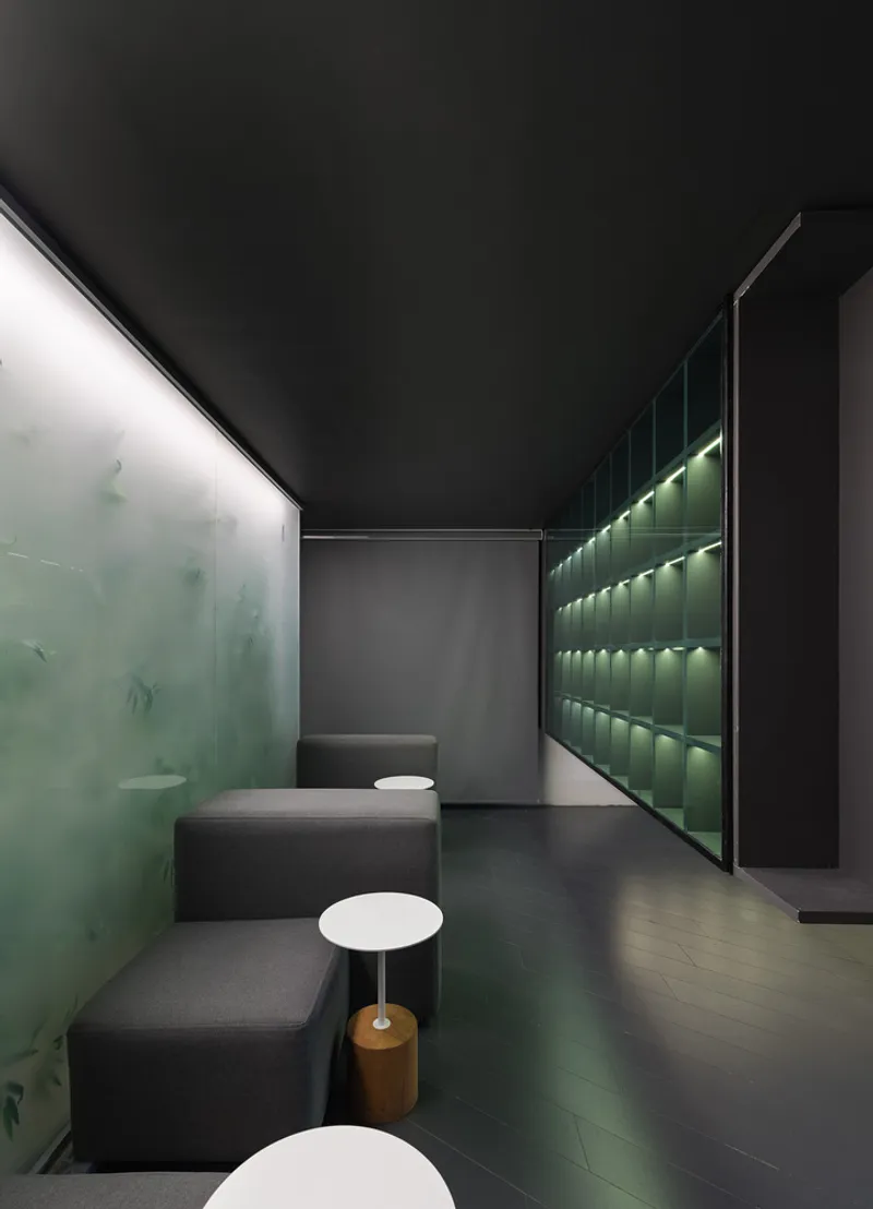 Seating area with backlit translucent green wall and illuminated display niches under a dark ceiling