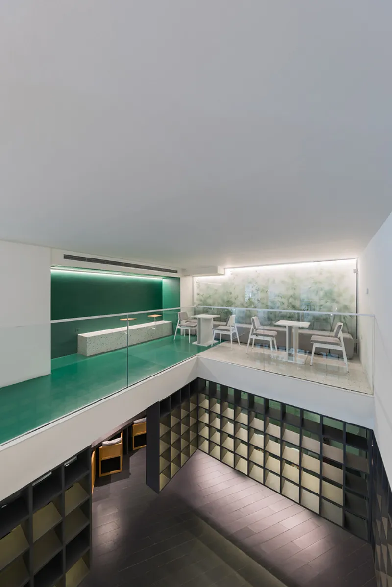 Double-height interior view showing a green upper kitchen level above a space with geometric grid wall