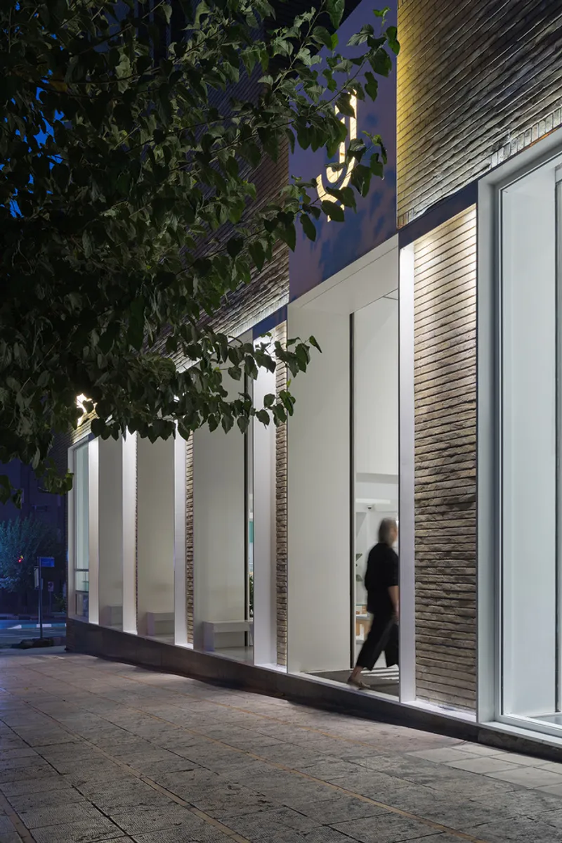 Street view at twilight showing glass shopfront with pedestrian walking past under illuminated signage