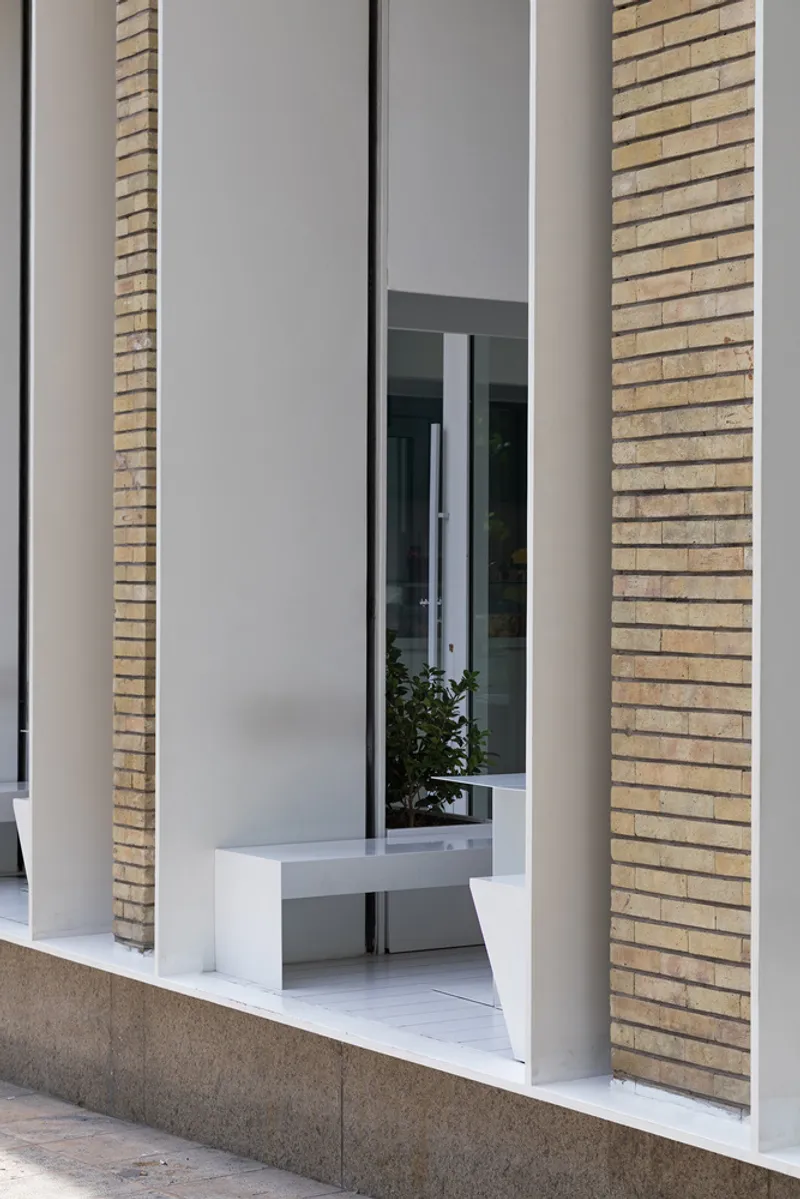 Entrance portal framed by buff-colored brick columns and white stucco with planter at threshold