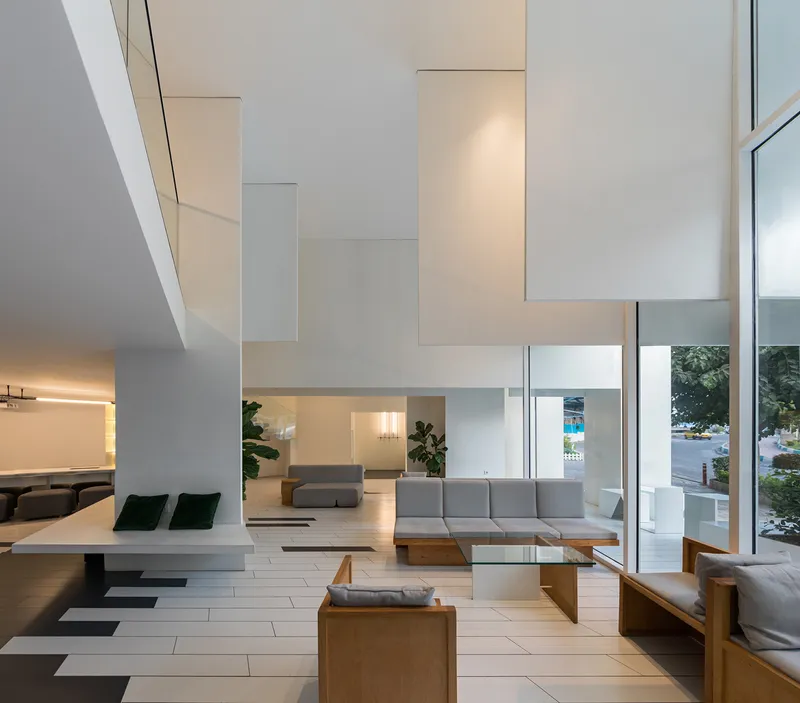 Double-height living room with white tile floor, floating staircase and floor-to-ceiling glazing overlooking greenery