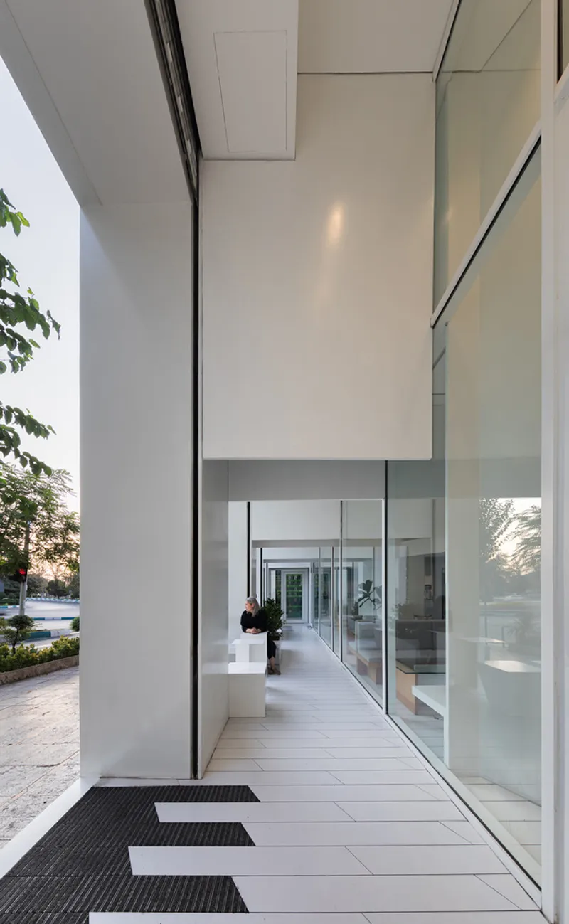 Covered entrance walkway with white tile paving, full-height glass walls and black entrance mats
