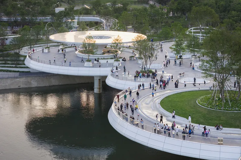 Elevated view of the curving white pedestrian paths crossing water with visitors gathered under the circular canopy