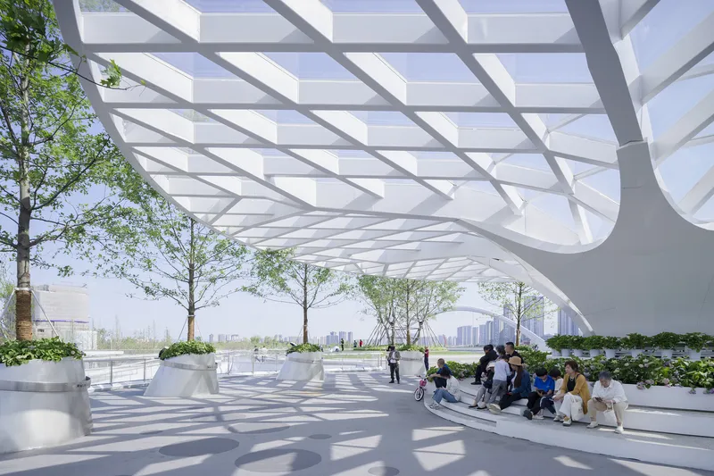 Covered terrace with white structural lattice overhead and visitors sitting among planters with trees