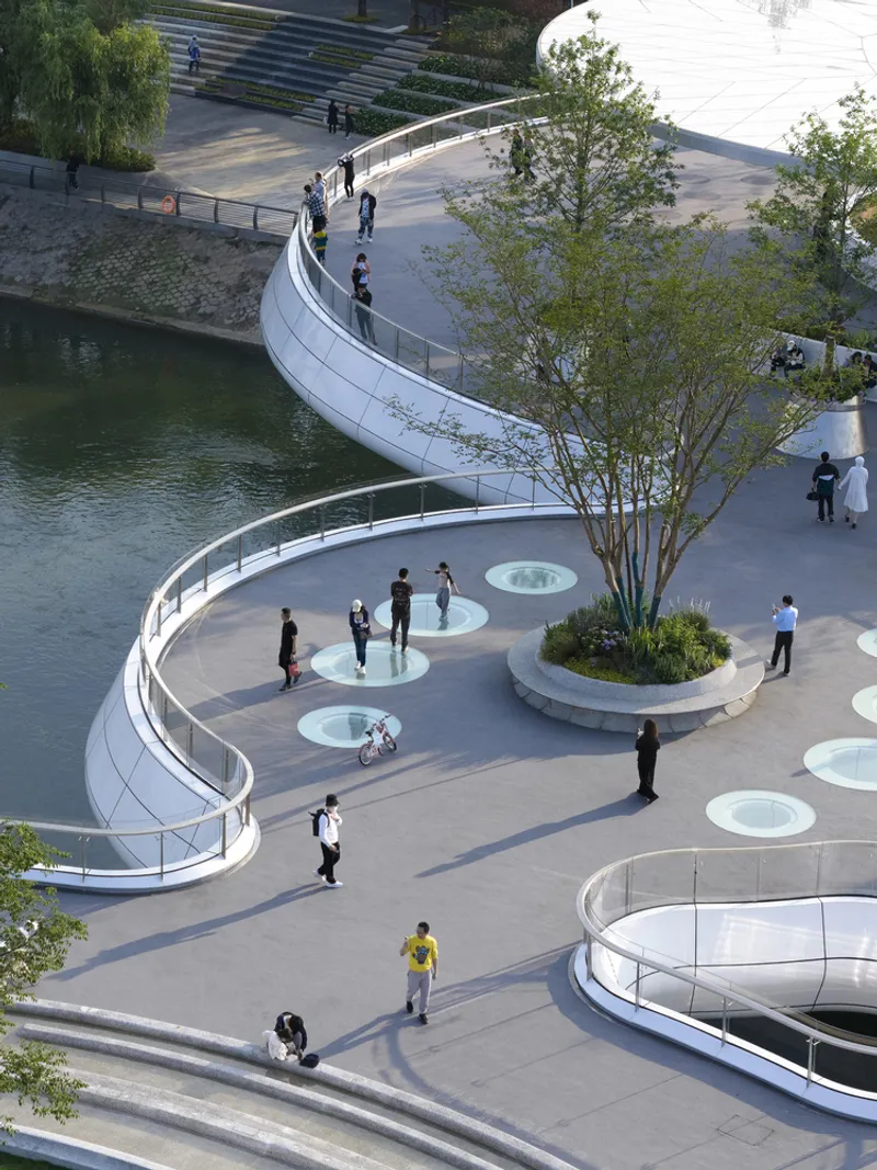 View from above showing the curved promenade with circular water features and planted beds between looping paths