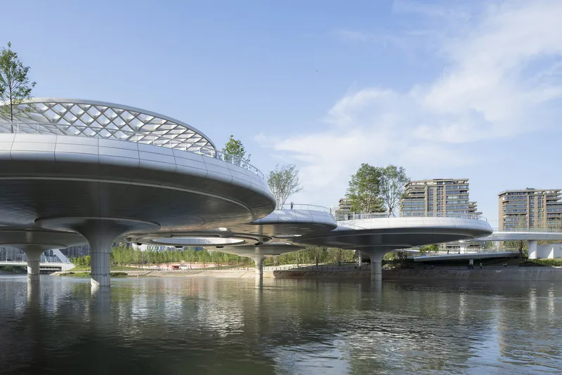 Elevated bridge decks with planted trees supported by cylindrical concrete columns rising from the waterway