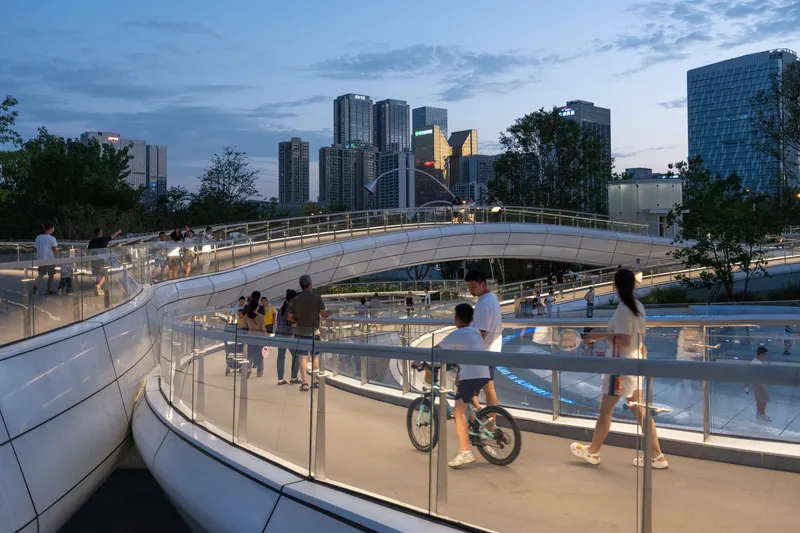 Spiraling pedestrian ramps with stainless steel railings connecting multiple levels at dusk