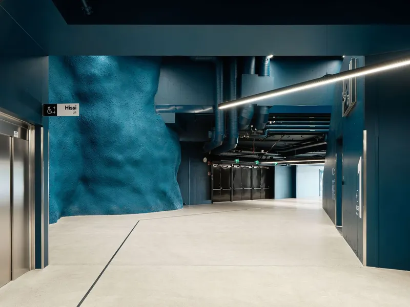 Interior hallway with painted blue rock wall and exposed ceiling services under linear lighting