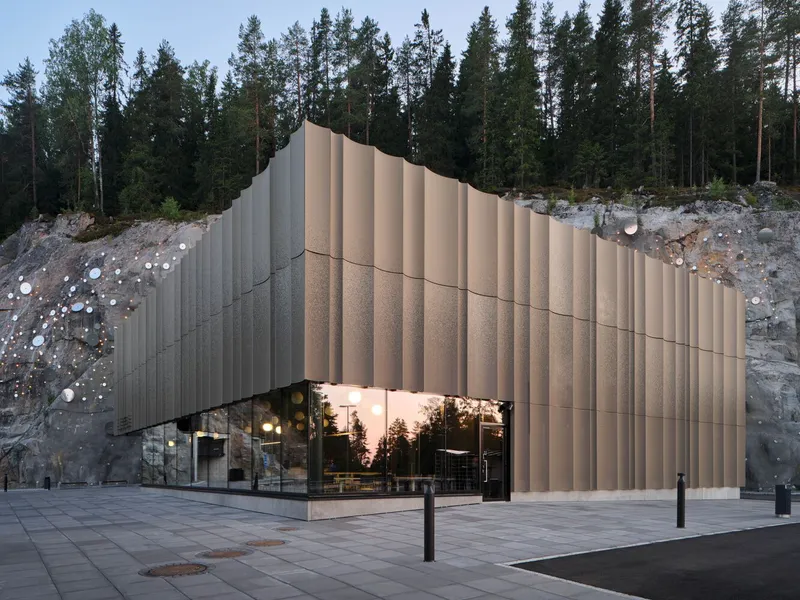 Corner view of the ribbed facade cantilevering above the glazed entrance at dusk
