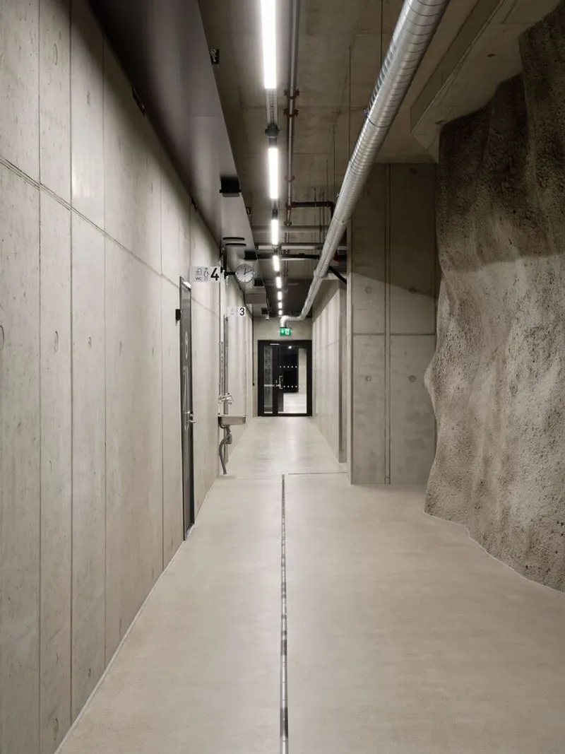Concrete corridor with exposed ductwork and formwork panels running alongside the raw rock wall