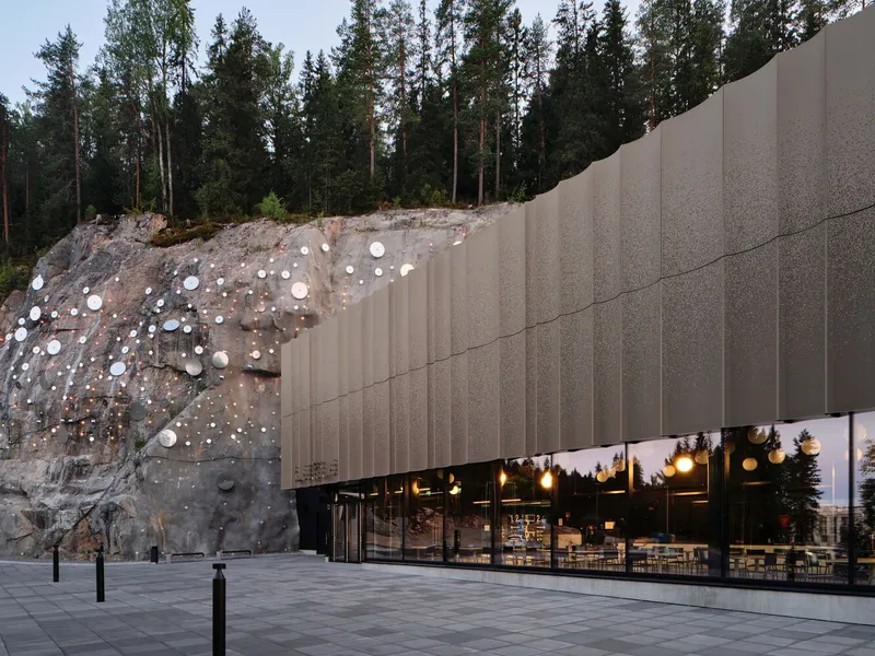 Glass-walled facade set against excavated rock studded with circular lighting elements at dusk